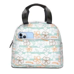 Op de afbeelding: Een witte lunchtas met een bloemenpatroon in tinten oranje, bruin en blauw. De tas heeft een ritssluiting en een zwarte handgreep. Er zit een klein vakje aan de voorkant van de tas met een blauwe telefoon erin.