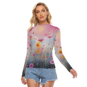 May include: A sheer, long-sleeved top featuring a floral print with pink, yellow, and purple flowers against a soft, pastel background. The top has a ruffled neckline and cuffs, and is paired with denim shorts.