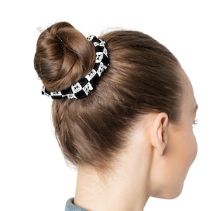 May include: A black and white patterned hair scrunchie with panda faces. The scrunchie is holding a woman's hair in a bun.