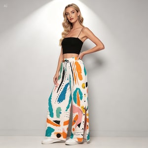 May include: A black spaghetti strap crop top paired with white wide-leg trousers featuring a multicolored abstract print in orange, teal, pink, and black. The trousers have a drawstring waist and side slits on the lower legs, worn with white sneakers.