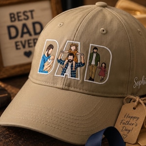May include: Khaki baseball cap embroidered with the word "DAD" and family illustrations. The cap features a curved brim and a top button. A framed picture behind the cap reads "BEST DAD EVER". A tag reads "Happy Father's Day!"