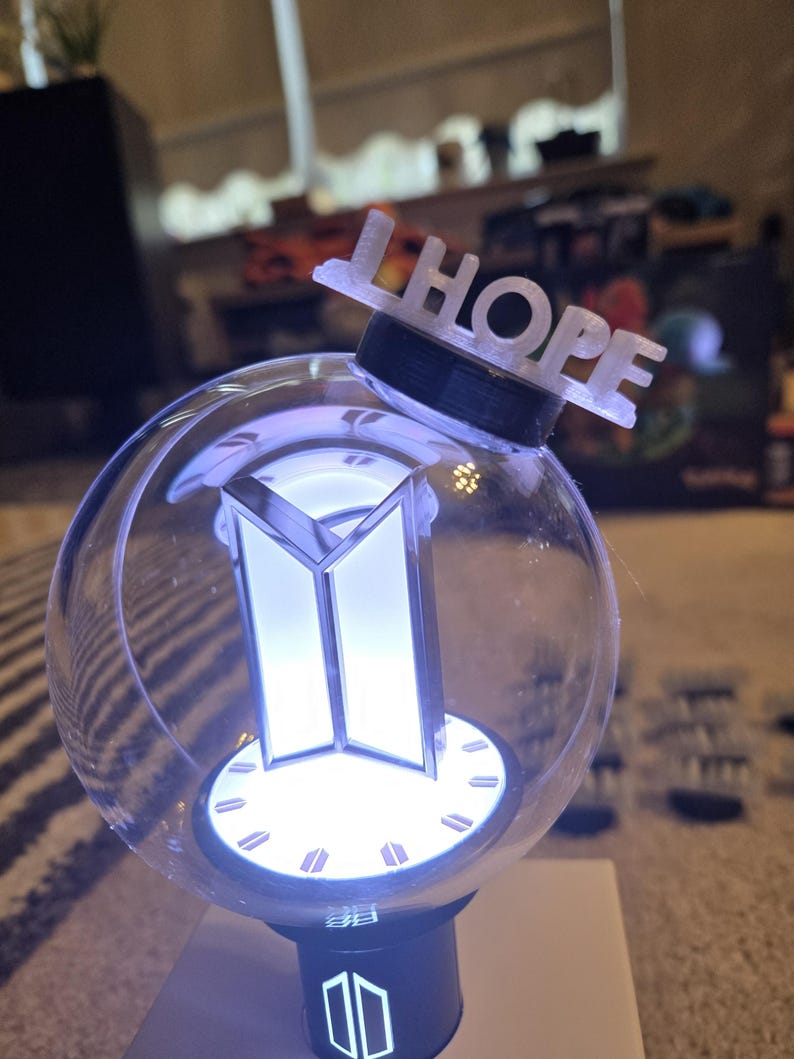 May include: A clear, spherical light-up device with a black base and a white, illuminated logo. The word "HOPE" is displayed on top. The device is designed to emit a soft, white glow.