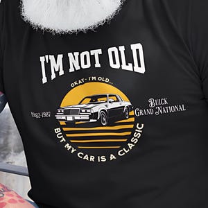 May include: Black t-shirt featuring the text "I'M NOT OLD" and "BUT MY CAR IS A CLASSIC". The design includes a Buick Grand National car graphic. The shirt also has the text "OKAY...I'M OLD" and "1982-1987".