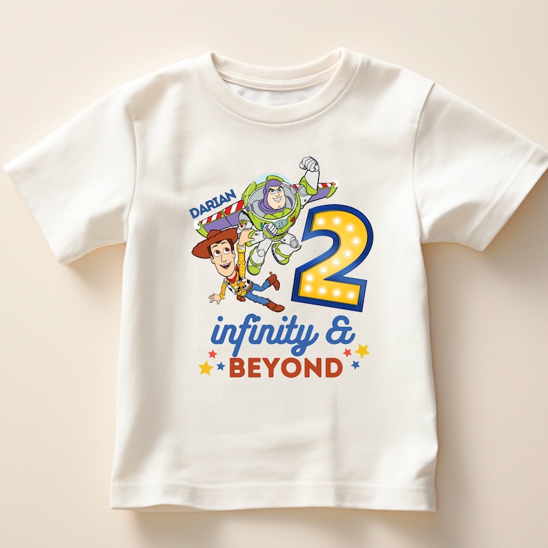 Puede incluir: Camiseta blanca de manga corta con un gr&aacute;fico colorido de Woody y Buzz Lightyear de Toy Story. El gr&aacute;fico incluye el n&uacute;mero "2", las palabras "infinity & BEYOND" y el nombre "DARIAN".