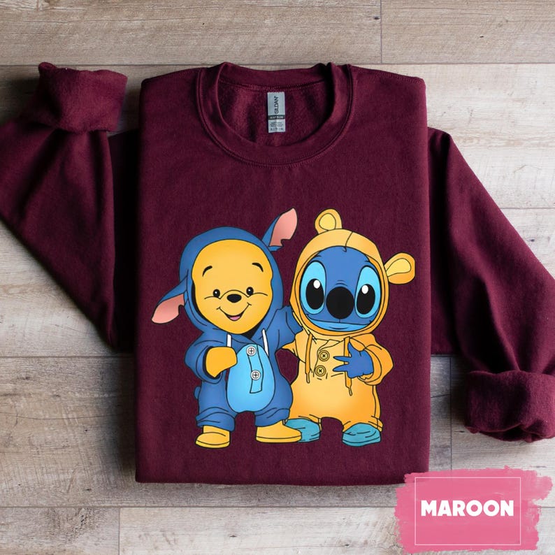 May include: Maroon sweatshirt with a graphic of Winnie the Pooh and Stitch wearing blue and yellow outfits. The characters are standing side by side and smiling.