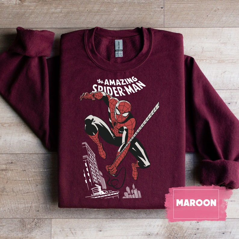 Pu&ograve; includere: Felpa color granata con un'immagine in stile fumetto vintage di Spider-Man che si dondola per la citt&agrave;. Il testo "the AMAZING SPIDER-MAN" &egrave; stampato sopra l'immagine.