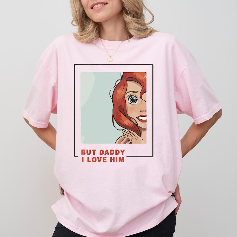 May include: Pink t-shirt featuring a cartoon image of a woman with red hair and the text "BUT DADDY I LOVE HIM" in a black frame.