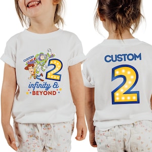 May include: White t-shirt with a blue and yellow number 2, a cartoon image of Woody and Buzz Lightyear from Toy Story, and the text "CUSTOM infinity & BEYOND". The back of the shirt has a blue and yellow number 2 with the text "CUSTOM".