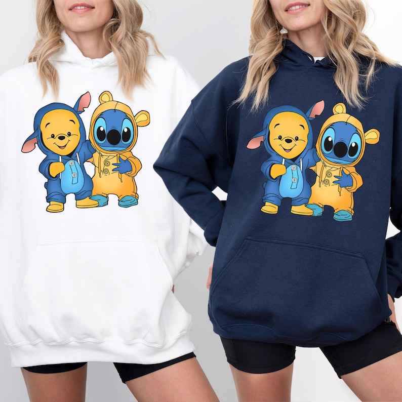 May include: Two white and navy blue hoodies with a graphic print of Winnie the Pooh and Stitch wearing matching outfits. The characters are in a cartoon style and are smiling.