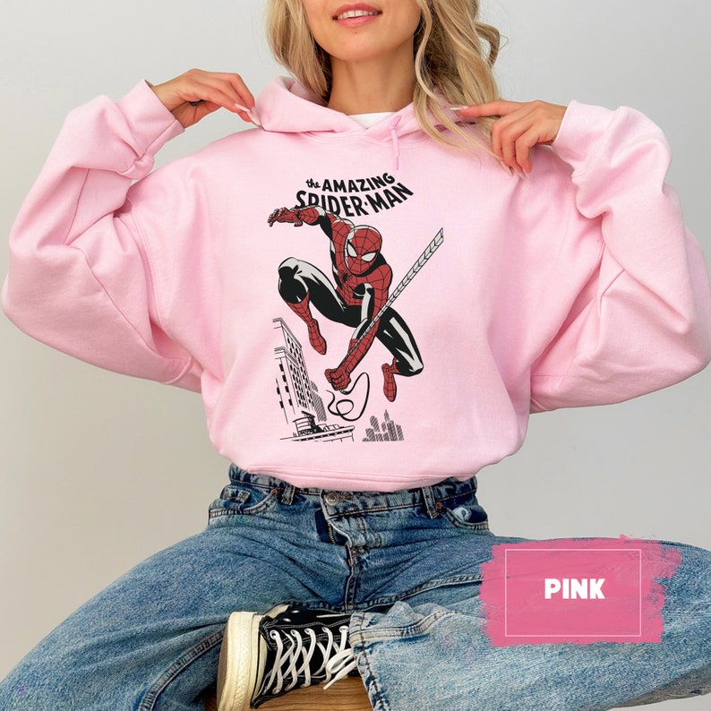 Pu&ograve; includere: Una felpa con cappuccio rosa con una grafica di Spider-Man sul davanti. La grafica dice "The Amazing Spider-Man".