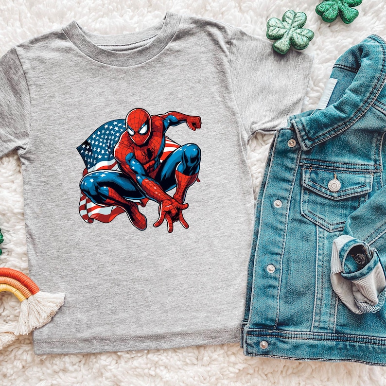 May include: A gray t-shirt featuring a graphic of Spider-Man in a crouching pose with an American flag design. A denim jacket and decorative shamrocks are also visible.