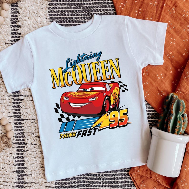 Puede incluir: Camiseta blanca con un gr&aacute;fico de Rayo McQueen, un coche de carreras rojo con el n&uacute;mero 95. La camiseta tiene el texto "Lightning McQueen" y "Think Fast".