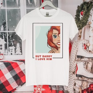 May include: White t-shirt featuring a cartoon image of a woman with red hair and the text "But Daddy I Love Him" printed on the front.