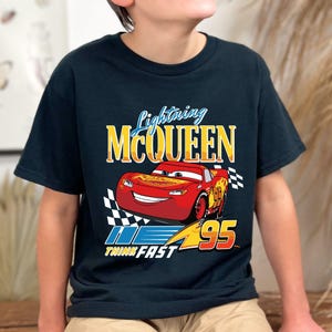 Puede incluir: Camiseta negra con Lightning McQueen de la pel&iacute;cula Cars. El dise&ntilde;o incluye un coche de carreras rojo, el texto "Lightning McQueen" y el n&uacute;mero "95". Tambi&eacute;n est&aacute; presente la frase "Think Fast".
