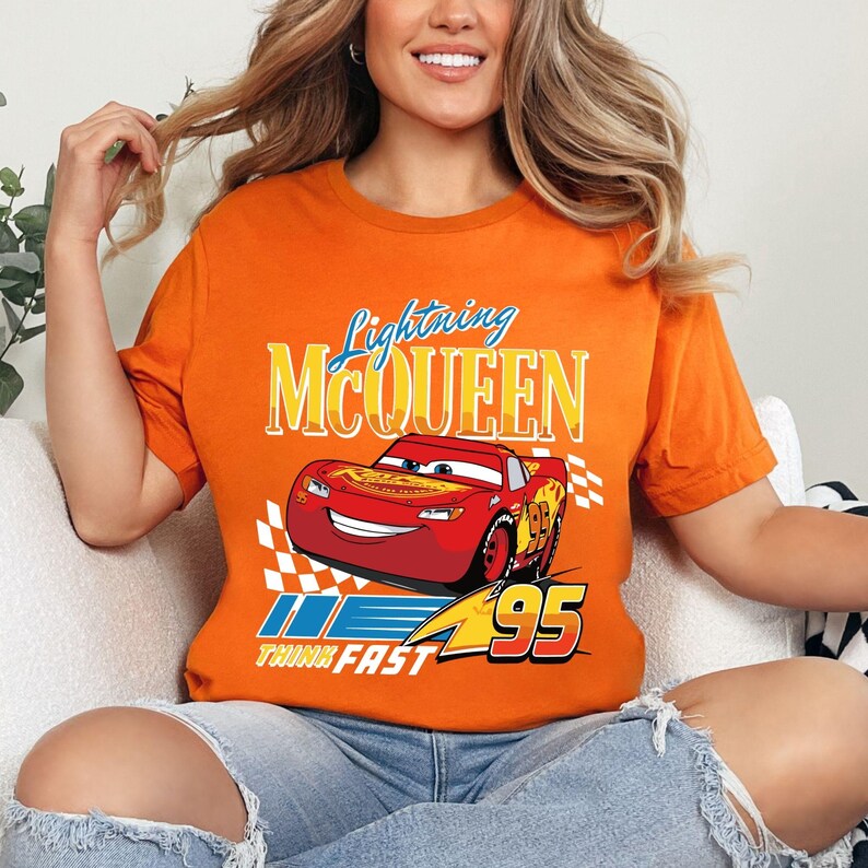 Puede incluir: Camiseta naranja con Lightning McQueen de la pel&iacute;cula Cars. El dise&ntilde;o incluye la imagen del personaje, el texto "Lightning McQueen" y el n&uacute;mero "95" con la frase "Think Fast". La camiseta es de un material suave.