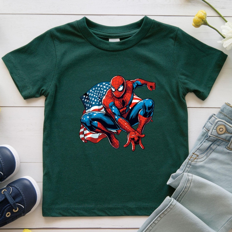 May include: A dark green t-shirt featuring a graphic of Spider-Man in a crouching pose with an American flag design in the background. The superhero is depicted in his classic red and blue suit.