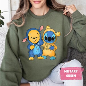 May include: A green sweatshirt with a cartoon image of Winnie the Pooh and Stitch wearing raincoats. The text "MILITARY GREEN" is in the lower right corner of the image.