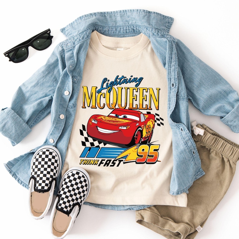 Puede incluir: Una camiseta crema con Lightning McQueen y el texto "Lightning McQueen" y "Think Fast 95". El conjunto incluye una camisa vaquera, pantalones cortos color caqui, zapatos sin cordones a cuadros y gafas de sol negras. Ropa para ni&ntilde;os.