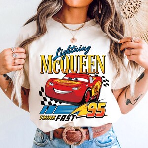 Puede incluir: Camiseta color crema con un dise&ntilde;o de Rayo McQueen, un coche de carreras rojo con el n&uacute;mero 95. El texto "Lightning McQueen" est&aacute; encima del coche y "Think Fast" debajo. Tambi&eacute;n hay una bandera a cuadros.