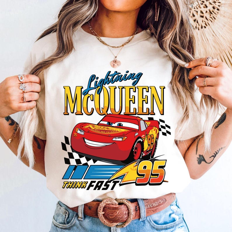 Puede incluir: Camiseta color crema con un dise&ntilde;o de Rayo McQueen, un coche de carreras rojo con el n&uacute;mero 95. El texto "Lightning McQueen" est&aacute; encima del coche y "Think Fast" debajo. Tambi&eacute;n hay una bandera a cuadros.
