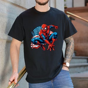 May include: Black t-shirt featuring a graphic of Spider-Man in a crouching pose with the American flag in the background. The superhero is depicted in his classic red and blue suit.