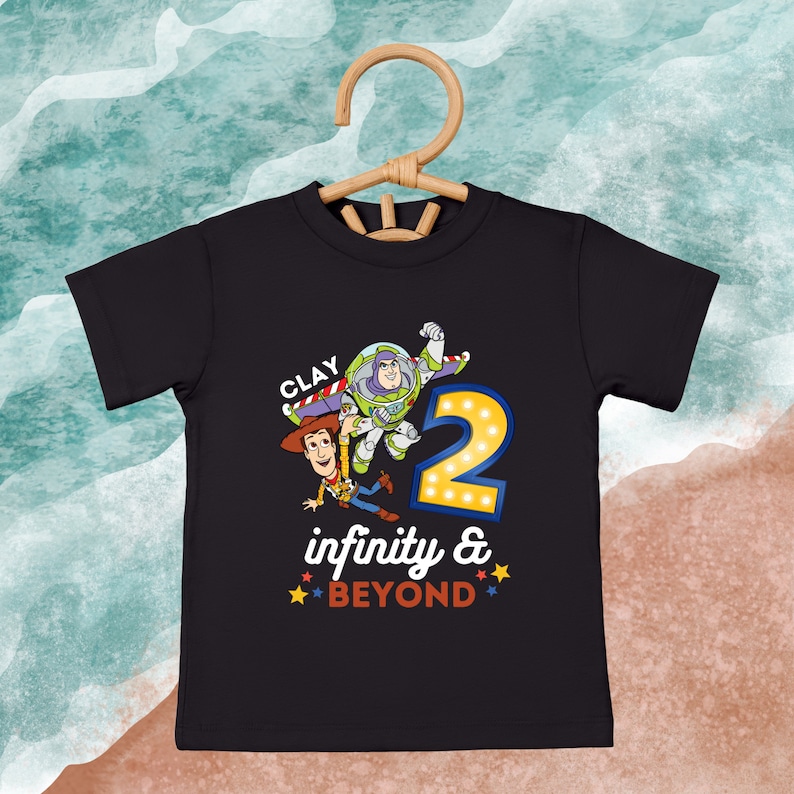 Puede incluir: Camiseta negra con un gr&aacute;fico de Woody y Buzz Lightyear de Toy Story. El gr&aacute;fico incluye el n&uacute;mero 2 con luces, el texto "CLAY" y la frase "infinity & BEYOND".