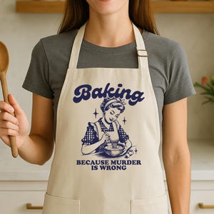 May include: Cream-colored apron with the word "Baking" in navy blue script. Below is a vintage illustration of a woman whisking in a bowl, with the text "BECAUSE MURDER IS WRONG". The apron has a bib and neck strap.