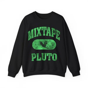 May include: Black crewneck sweatshirt with the words "Mixtape Pluto" in distressed green lettering. A green oval in the center features a silhouette of a flying eagle. The sweatshirt is a casual, unisex garment.