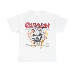 May include: White t-shirt with a graphic skull design and the text "OSAMASON". The design is in red, white, and yellow. Two small cartoon figures are below the skull on a line. The shirt has a crew neck.