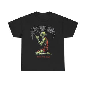 Op de afbeelding: Zwart T-shirt met een knielend skelet in een rood gewaad. De tekst "REST IN BASS" staat boven het skelet en "BRING THE NOISE" eronder. Het skelet is groen en geel.