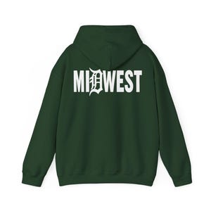 Puede incluir: Sudadera con capucha verde oscuro con la palabra "MIDWEST" impresa en blanco en la espalda. La "D" de "MIDWEST" tiene un diseño estilizado. La sudadera tiene capucha y mangas largas.