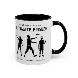 Peut inclure: Mug en céramique blanche avec intérieur et anse noirs. Le mug présente le texte "FUNDAMENTALS OF ULTIMATE FRISBEE" au-dessus de silhouettes de personnes jouant au frisbee. Le texte "BACKHAND.. FOREHAND.. BEERHAND!" est imprimé en dessous.