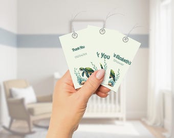 May include: Two white thank you tags with a green sea turtle design. The text on the tags reads "Thank You 05/04/XX" and "Elizabeth's Shower Thank You".