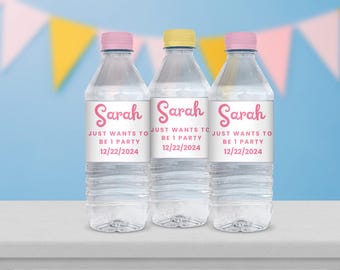 Puede incluir: Tres botellas de agua de plástico transparente con etiquetas personalizadas. Las etiquetas son blancas con texto rosa que dice "Sarah Just Wants To Be 1 Party 12/22/2024".