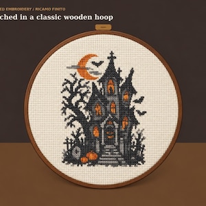 Può includere: Un ricamo finito in un classico telaio in legno con un disegno a punto croce di una casa stregata, una luna crescente, pipistrelli e zucche. Il testo recita: FINISHED EMBROIDERY / RICAMO FINITO Stitched in a classic wooden hoop.
