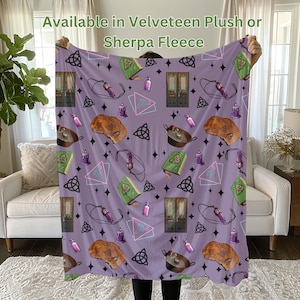 Può includere: Coperta in pile viola con un motivo ripetitivo di un calderone, un libro, una bottiglia, una candela, una stella, una porta e un triangolo. Il testo "Available in Velveteen Plush or Sherpa Fleece" è in cima alla coperta.