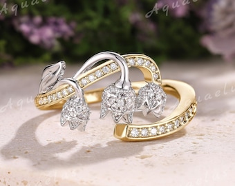 May include: A two-tone ring featuring a floral design. The ring has a gold band with a row of small, clear stones. The floral design has three flower buds with clear stones and a silver stem.