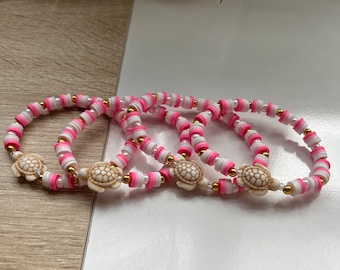 May include: Four pink and white beaded bracelets with gold accents and a small turtle charm on each.