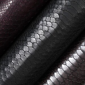 May include: Three rolls of textured material featuring a repeating scale pattern. The rolls are arranged diagonally, displaying deep shades of dark purple, black, and a muted charcoal gray, each with a glossy finish and distinct embossed texture.
