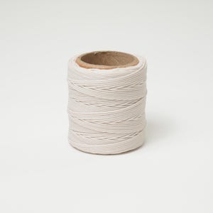 May include: A spool of off-white cord, tightly wound around a cardboard core. The cord appears to be made of a synthetic material. The spool is cylindrical and sits on a white background. The cord is suitable for crafting and general use.