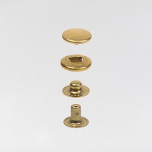 May include: A disassembled brass snap fastener, showcasing its four components: a cap, a socket, a stud, and a post. The parts are arranged vertically, displaying their individual shapes and textures. The components are made of brass.