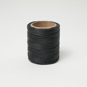 May include: A spool of black waxed thread, tightly wound around a cardboard core. The thread appears smooth and durable, suitable for various crafting projects. The spool is cylindrical and sits against a plain white background.
