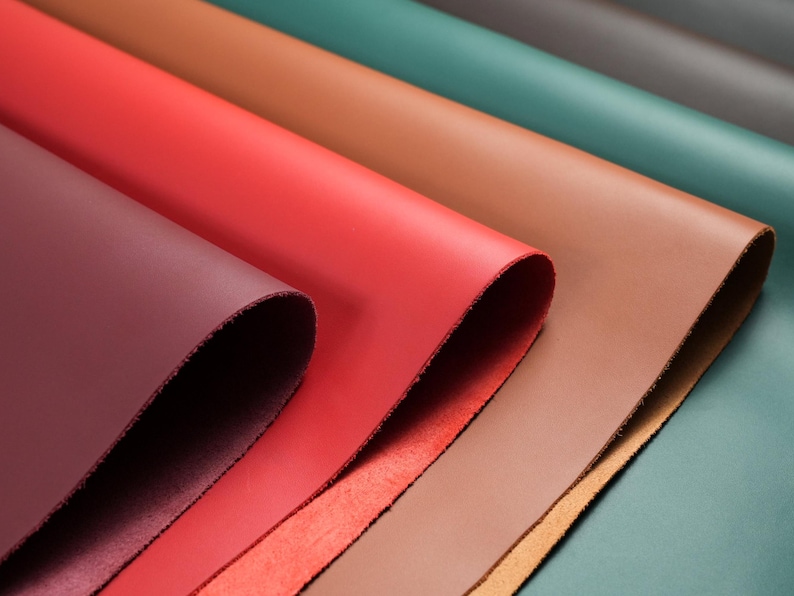 A top view of folded top grain premium Italian leather, 4.5-5 oz, in various colors: brown, black, green, red, burgundy, and cognac brown—perfect for crafting projects.