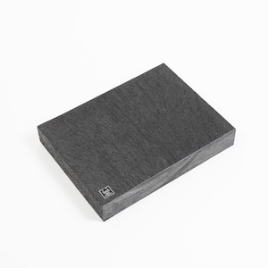 May include: A rectangular, dark gray wooden board with a textured surface. The board has a subtle wood grain pattern and a small, square logo in the lower corner. The board is set against a white background.