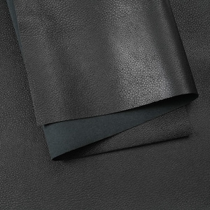 May include: A sheet of black leather with a distinct pebbled texture. The material is folded over to reveal a smooth, matte dark gray underside, contrasting with the textured, grainy surface of the top layer of the leather hide.
