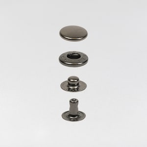 May include: An exploded view of a dark gray metal snap fastener, showing the cap, socket, stud, and post components. The components are arranged vertically against a white background, highlighting the details of each piece.