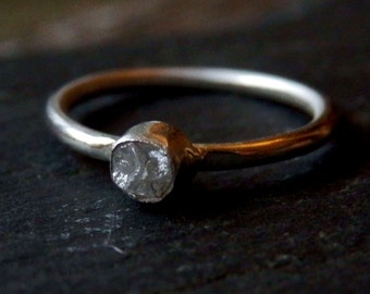 May include: A silver ring with a single, clear, faceted gemstone set in the center.