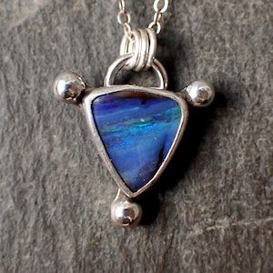 May include: A silver necklace with a triangular pendant featuring a blue opal gemstone. The pendant has three silver balls on each corner.