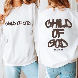 Puede incluir: Sudadera blanca con la inscripción "CHILD OF GOD" impresa en marrón en la parte delantera y trasera. La parte trasera también presenta "PSALM 23". Una prenda superior informal de manga larga para el uso diario.