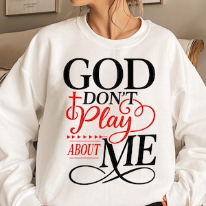 May include: White sweatshirt with the text "GOD DON'T PLAY ABOUT ME" in black and red. The word "GOD" is in a bold font, and the word "PLAY" is in a script font. The sweatshirt is a casual style.